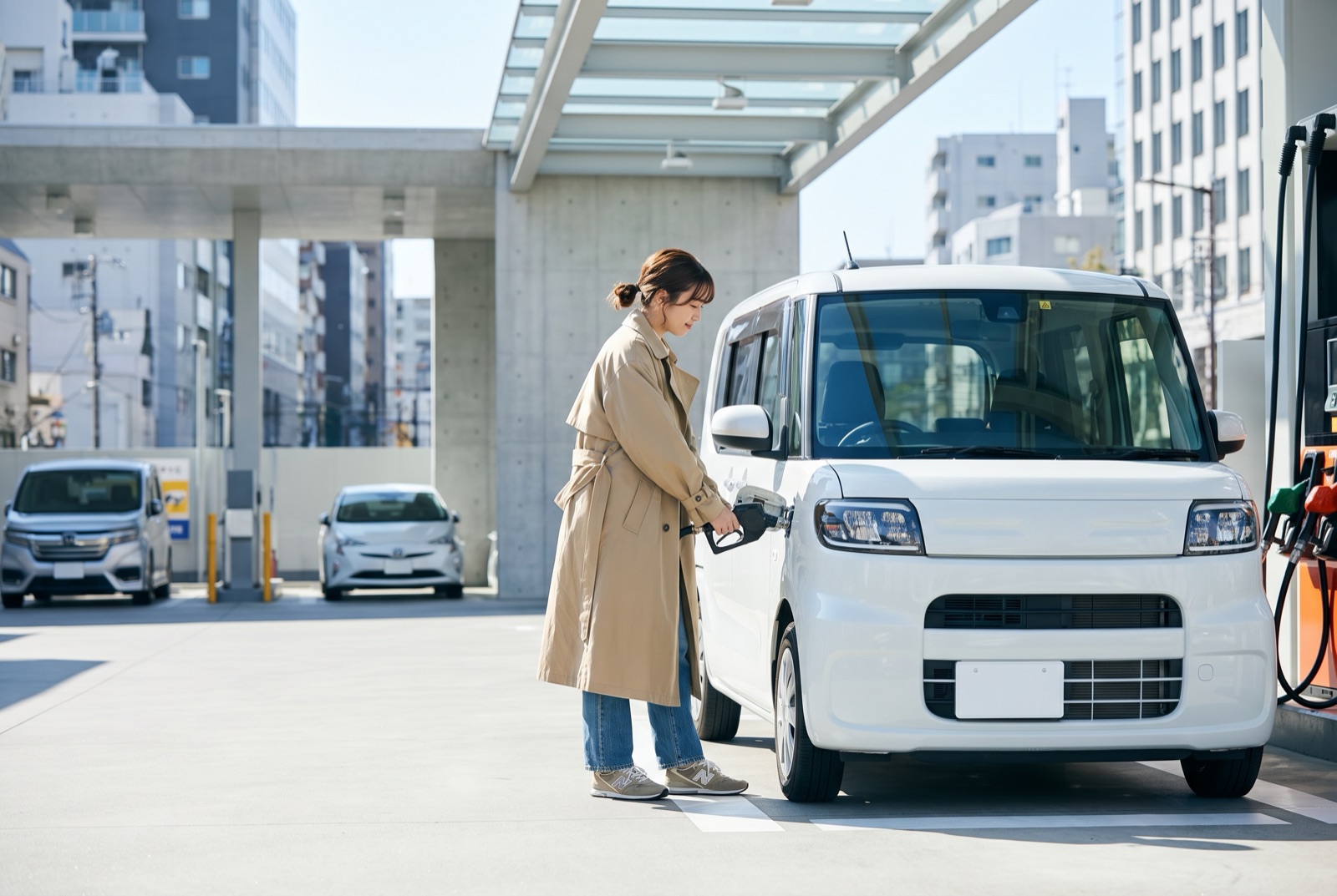 セルフのガソリンスタンドで軽自動車に給油する若い女性