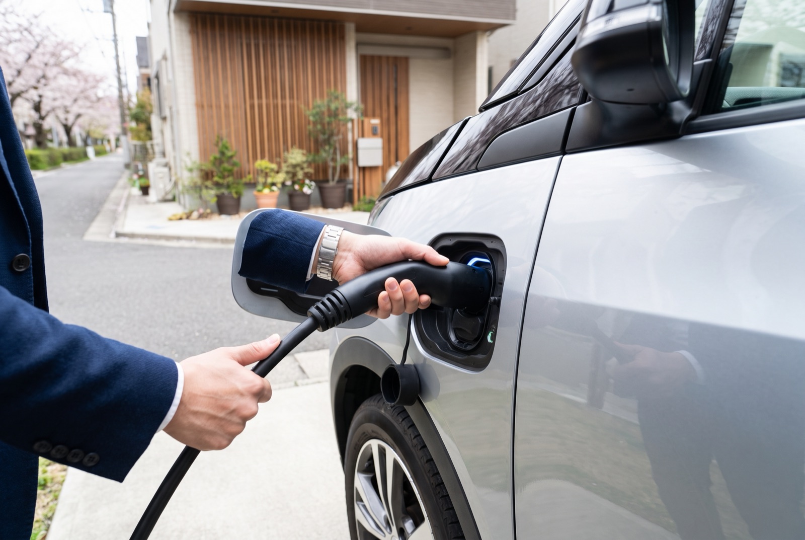 戸建ての駐車場でEVの充電ポートにケーブルを差し込む手元