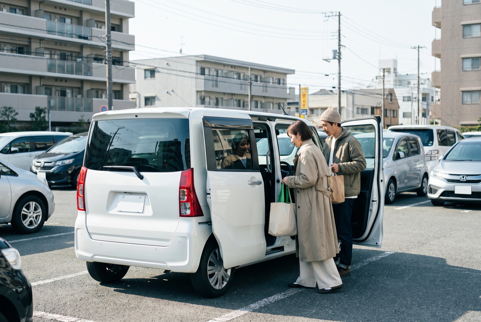 駐車場で軽ワゴンのスライドドアから買い物袋を積み込む二人連れの様子