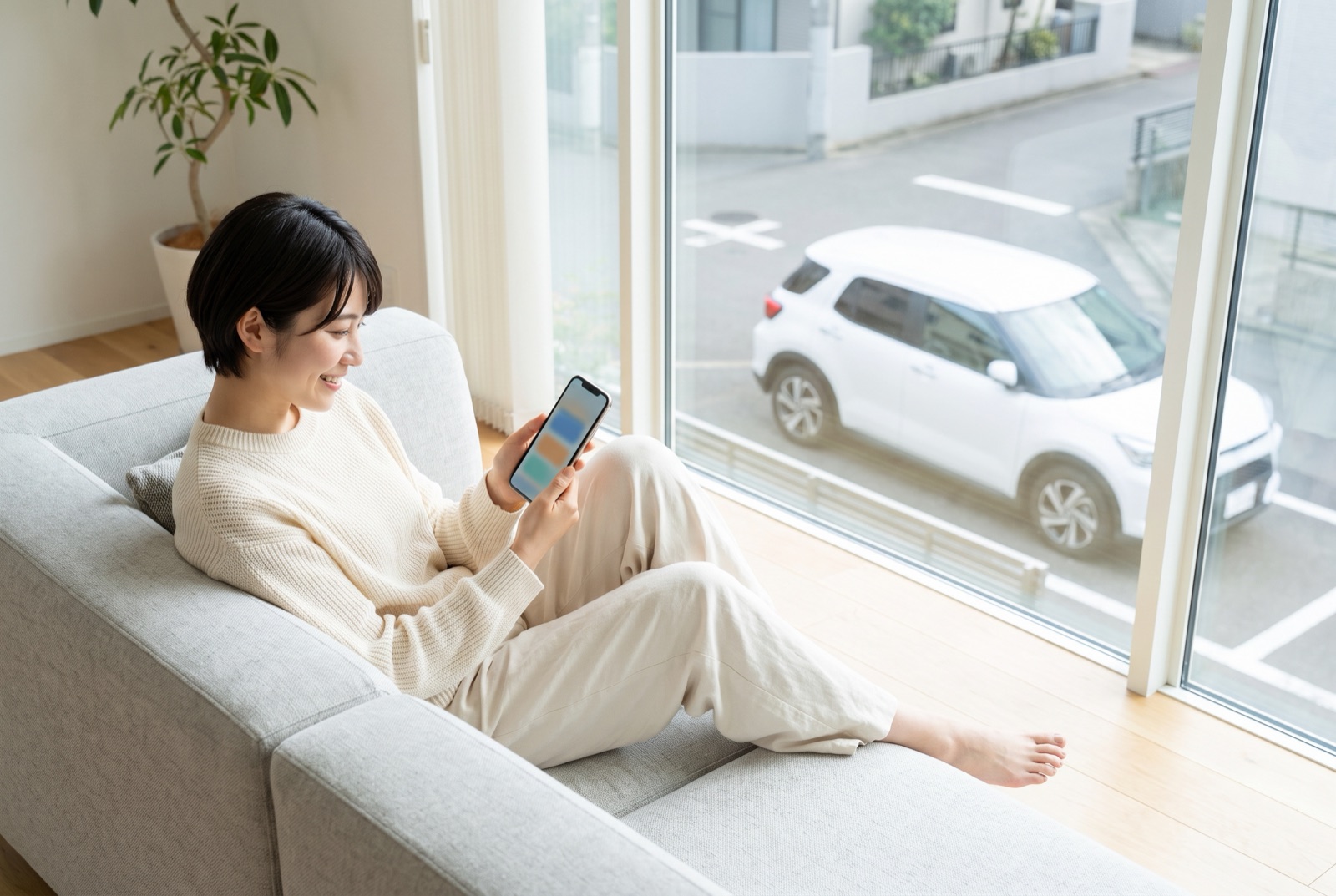 ソファでスマートフォンを見ながらクルマのサブスクを検討する女性