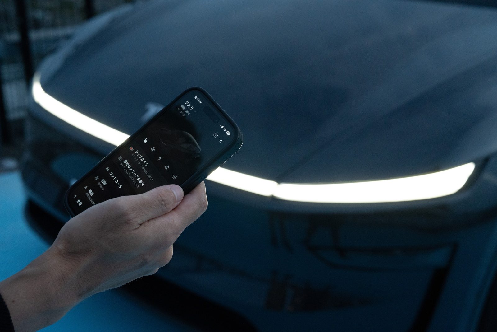 モデルYの前でテスラアプリを表示したスマートフォン
